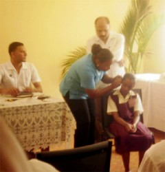 Minister of Health Dr Bheri Ramsaran (standing) looks on as a nurse fits a child with a hearing aid.