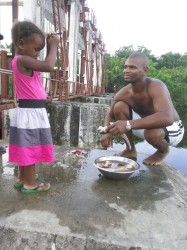 Richardo Harris (my brother-in-law) cleans some fish he caught while his daughter Genisa looks on at the GuySuCo five gate compound at Bartica