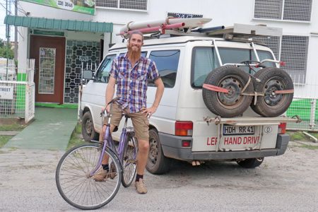 Roman Rominger in front of his trusty Volkswagen van. He has used his surf board, which sits is atop his van, to surf the waters of India and several of the other countries he has visited. He uses his bicycle to get around the cities he visits.
