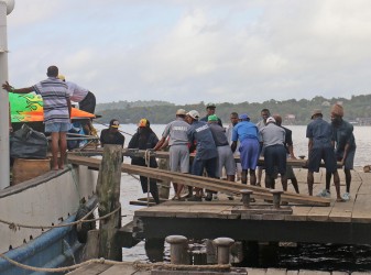 Prisoners helping to position planks for the offloading of this boat at the Bartica Stelling yesterday. (Arian Browne photo)