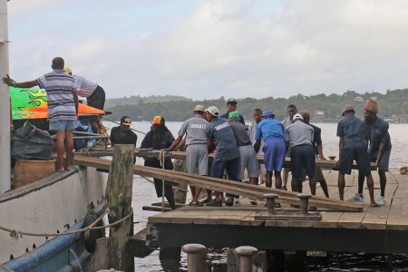 Prisoners helping to position planks for the offloading of this boat at the Bartica Stelling yesterday. (Arian Browne photo)
