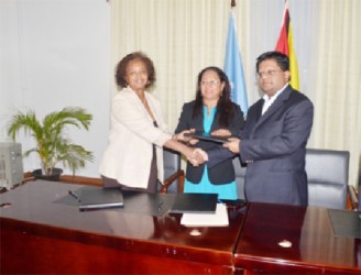 United Nations Development Programme (UNDP) Resident Representative and UN Coordinator Khadija Musa and Minister of Finance Dr. Ashni Singh shake hands after signing the $1.3B agreement, while Minister of Amerindian Affairs Pauline Sukhai looks on. (Government Information Agency photo) 