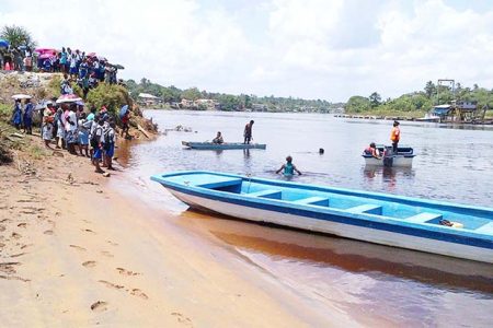 Boats and divers searching the Demerara River for Omar Mitchell yesterday while relatives and others look on. (Photo by Jeff Trotman)