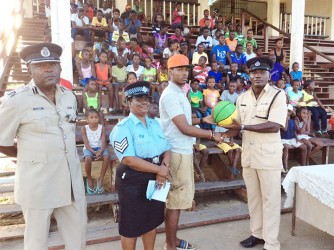 Assistant Superintendent Joshua Harvey-John hands over a basketball to captain of the team Fonsie James in the presence of Assistant Commissioner Brian Joseph and Sergeant Cynthia Kelly 