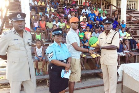 Assistant Superintendent Joshua Harvey-John hands over a basketball to captain of the team Fonsie James in the presence of Assistant Commissioner Brian Joseph and Sergeant Cynthia Kelly 