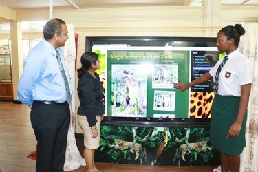 Administrator (ag) Ms Nadia Madho (centre) and student Rojeria McWatt try one of the touchscreens while Culture Minister Frank Anthony looks on. 