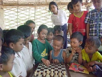 The most popular chess game in Cambodia is the Ouk Chatrang , a board game similar to chess in a way, but still with some notable differences. Neighbouring countries such as Thailand and Vietnam participate in the Chess Olympiads, but Cambodia has never developed the game of chess to oppose her neighbours. Bolon has noted that developing chess activity in Cambodia will allow the country to get official status from FIDE and to participate in tournaments around the world. In the photo, students pay rapt attention to one of their own as she explains how the pawn moves.