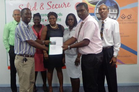  Assuria General Manager (Ag) Yogindra Arjune (second from right) presents a copy of the Guyana Teachers Union (GTU) agreement to GTU president Mark Lyte while representatives from both entities: Clyde Muntslag, Coretta McDonald, Eulalie Wilson, Lesmeine Collins and Erwin Daniels look on. 