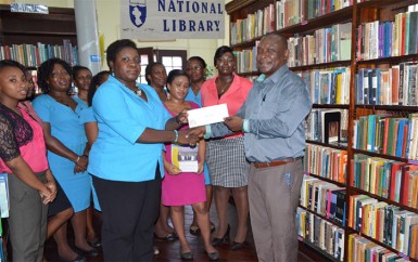 Emily King, Chief Librarian (ag.) receives the cheque from Troy Peters (right) , Banks DIH  Limited Communications Manager in the presence of staff of the library. (Banks DIH photo)