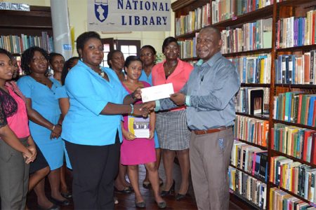 Emily King, Chief Librarian (ag.) receives the cheque from Troy Peters (right) , Banks DIH  Limited Communications Manager in the presence of staff of the library. (Banks DIH photo)