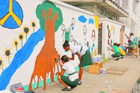 Art wall: Students of St Roses High in collaboration with Guyana Shines painting a mural on their school wall yesterday to depict keeping the environment clean among other positive messages. (Photo by Arian Browne)
