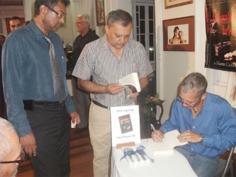 Hans Gaskin (seated) signs a copy of his book The Ashgabat Verdict for CEO of the Georgetown Public Hospital (GPH) Michael Khan (centre) while MP Khemraj Ramjattan waits his turn 