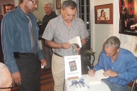 Hans Gaskin (seated) signs a copy of his book The Ashgabat Verdict for CEO of the Georgetown Public Hospital (GPH) Michael Khan (centre) while MP Khemraj Ramjattan waits his turn
