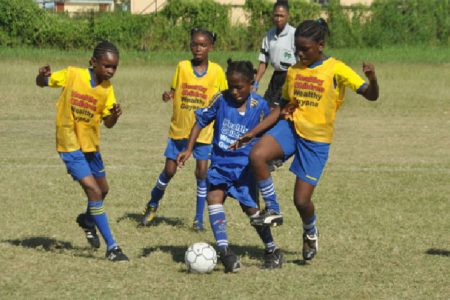 Aaliyah Elaine of Enterprise Primary (centre/blue vests) attempting evade challenges from two St. Pius Primary defenders during her side’s 4-0 win
