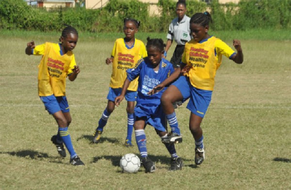 Aaliyah Elaine of Enterprise Primary (centre/blue vests) attempting evade challenges from two St. Pius Primary defenders during her side’s 4-0 win 
