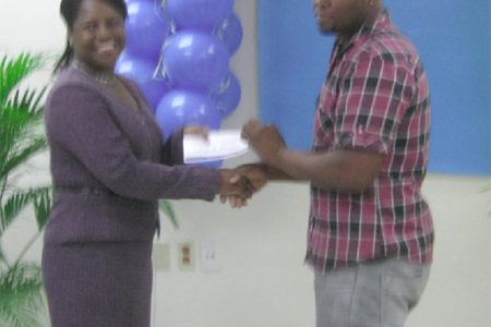 Republic Bank’s Finance and Production Manager Vanessa Thompson presents first place winner Eon Rodney with his prize 