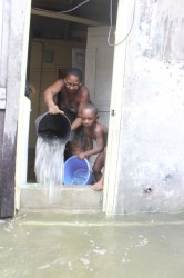 Myrtle Hinds and her five-year-old grandson bailing out water from their home yesterday. 