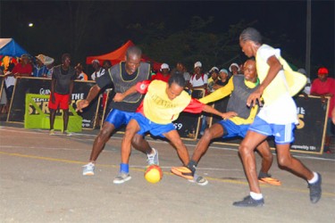 Kacy John (centre/yellow vest) of East Front Road battling to maintain possession of the ball while being challenged by North Sophia defenders during their side’s matchup 