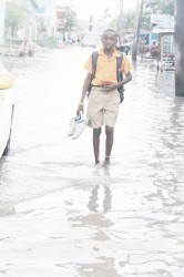 A schoolboy carries his shoes as he makes his way through one of the waterlogged streets in Albouys-town on Tuesday. (Photo by Arian Browne)