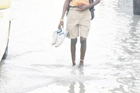 A schoolboy carries his shoes as he makes his way through one of the waterlogged streets in Albouys-town on Tuesday. (Photo by Arian Browne)