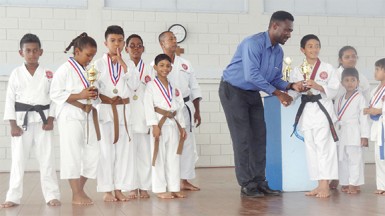 Sports Coordinator of the Marian Academy Chris Bowman handing over a trophy to Karateka Zachary Persaud 