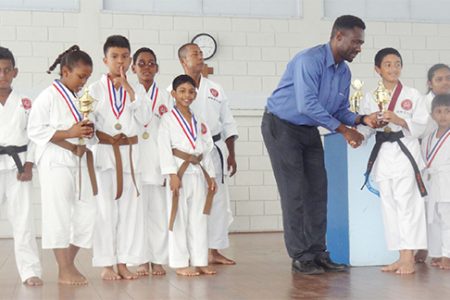 Sports Coordinator of the Marian Academy Chris Bowman handing over a trophy to Karateka Zachary Persaud
