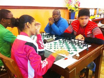 Suriname’s Woman Candidate Master Reyna Frijde faces Guyanese Roberto Neto at the start of their round six encounter at the 2014 Guyana Umada Chess Cup. Playing the advantageous white pieces, Reyna out-manoeuvred her opponent to seize the full point. Sitting next to Roberto is Candidate Master Ronuel Greenidge who represented Guyana diligently at the 2014Tromso Chess Olympiad in Norway. Ronuel’s opponent is Wendell Muesa who contested the tournament under the Barbadian flag.