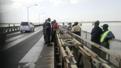 Police officers and Demerara Harbour Bridge Corporation officials standing at the spot where the unidentified woman jumped to her death yesterday, off the Demerara Harbour Bridge. 