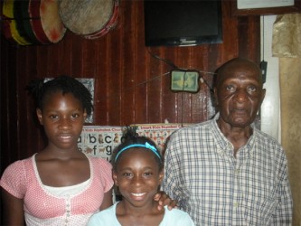 Jerome ‘Three Feet’ Cumberbatch and two of his youngest band members in his Linden home. Monica Stewart (centre) and Serena Lambert (left) are both 12 years old