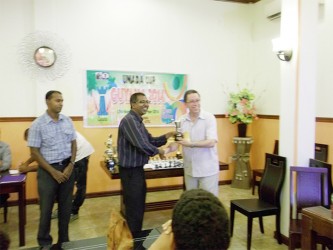 The World Chess Federation’s Caribbean representative Alan Herbert (right) presents the Under-1700 trophy for Excellence to Loris Nathoo at the closing ceremony of the 2014 Guyana Umada Chess Cup recently. Herbert acted as FIDE’s representative for the organization’s president, Kirsan Ilyumzhinov. The conclusion of World Championship title match between Carlsen and Anand in Russia, clashed with the finish of the Umada Cup, thereby preventing Ilyumzhinov from attending the Guyana closing ceremony.  Nathoo was adjudged the best U-1700 player of the tournament from the five participating countries, although he missed the first round of the competition. President of the Guyana Chess Federation Irshad Mohammed is at left. 