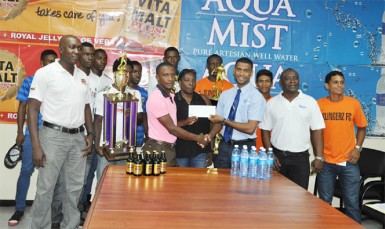 WDFA President Nigel Garraway (centre) receives the cheque from Aqua Mist Brand Manager Errol Nelson (3rd from right) while Vita Malt Brand Manager Clayton McKenzie (1st from left), Communications Manager Troy Peters (2nd from right), players and WDFA officials look on 