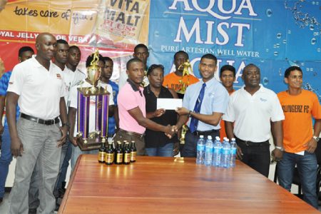 WDFA President Nigel Garraway (centre) receives the cheque from Aqua Mist Brand Manager Errol Nelson (3rd from right) while Vita Malt Brand Manager Clayton McKenzie (1st from left), Communications Manager Troy Peters (2nd from right), players and WDFA officials look on