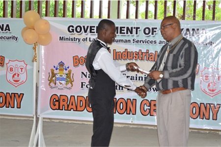 Minister in the Ministry of Finance, Juan Edghill presents a certificate to one of the Linden graduates (GINA photo)