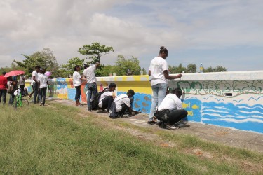 The Green Ambassadors of the Environmental Community Health Organisation painting murals along the Kitty seawall yesterday to encourage the public to keep Guyana green and beautiful.