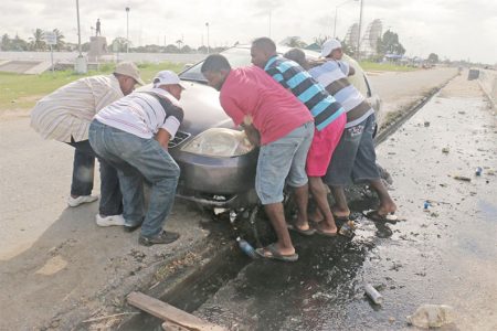 A helping hand: These men came together on Tuesday to help this driver whose vehicle ended up in the drain along the Kitty seawall.