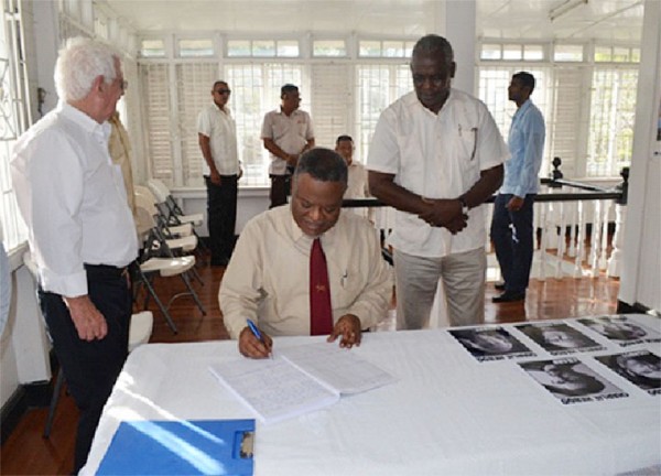 Prime Minister Samuel Hinds yesterday signing the Book of Condolence opened at the French Consulate in Queenstown for the victims of the Charlie Hebdo attack in Paris last week in which cartoonists were killed by terrorists. Public Works Minister Robeson Benn  (standing at right)  and Deputy French Consul, David Bertilli (left) are also in this GINA photo.