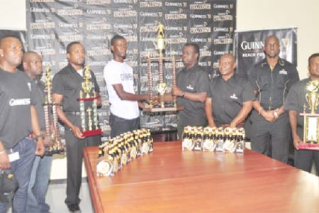 Joint tournament coordinator Travis Best (fourth from left) receives the championship trophy from Banks DIH representative Ezequiel Beard while other members of the company look on. 