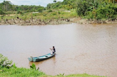 A young boy paddles his boat in the creek 