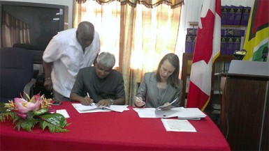 Chairman of the Guyana Elections Commission Dr Steve Surujbally (left) and Canadian High Commissioner Dr Nicole Giles (right) sign the agreement for the release of CDN$43,360 to purchase laptops to assist in the electoral process as Chief Election Officer Keith Lowenfield looks on from behind.  