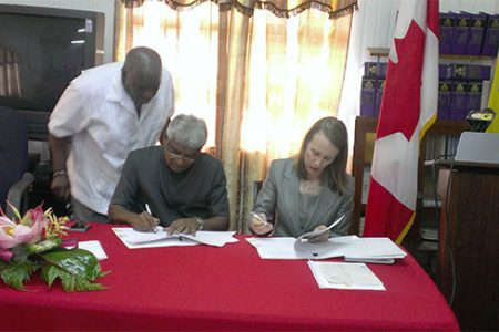 Chairman of the Guyana Elections Commission Dr Steve Surujbally (left) and Canadian High Commissioner Dr Nicole Giles (right) sign the agreement for the release of CDN$43,360 to purchase laptops to assist in the electoral process as Chief Election Officer Keith Lowenfield looks on from behind.