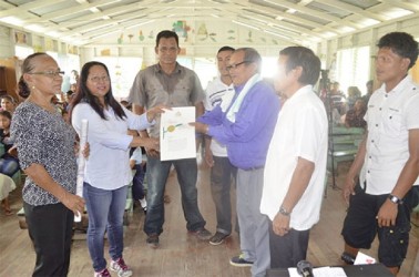 Minister of Amerindian Affairs Pauline Sukhai handing over the title document to Toshao of Kariako Lewis Samuels in the presence of Liaison to the Ministry Yvonne Pearson and residents of Kariako. (Government Information Agency photo) 