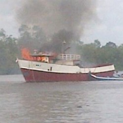 A small boat guiding the burning trawler 