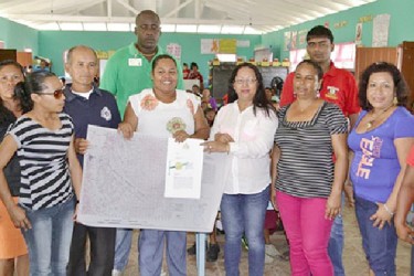 Toshao of Riverview, Melinda Pollard (fourth from right in foreground) receiving the community’s land title document from Minister of Amerindian Affairs, Pauline Sukhai. (GINA photo)   