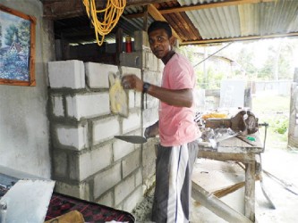 19-year-old Amarnauth Narassiah plastering a concrete wall he erected to extend his family home