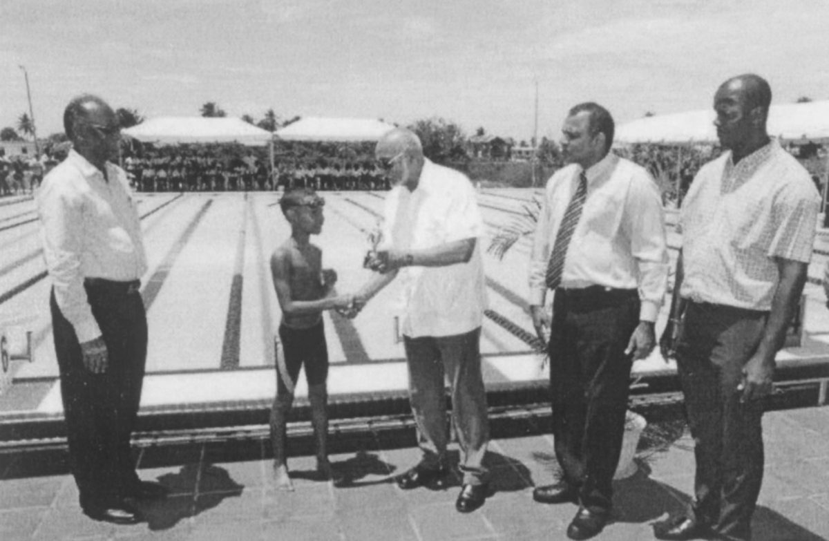 Director of Sports Neil Kumar, left, Dr. Frank Anthony, second right and Permanent Secretary Alfred King, right watches as President Donald Ramotar presents a trophy to the winner of an exhibition race at the newly commissioned Warm Up pool Friday at the National Aquatic Centre, Liliendaal. (photo courtesy of GINA)


