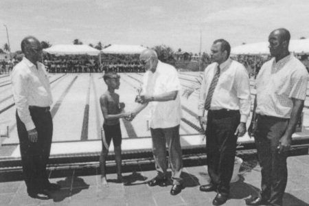 Director of Sports Neil Kumar, left, Dr. Frank Anthony, second right and Permanent Secretary Alfred King, right watches as President Donald Ramotar presents a trophy to the winner of an exhibition race at the newly commissioned Warm Up pool Friday at the National Aquatic Centre, Liliendaal. (photo courtesy of GINA)