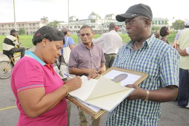 A woman takes time out from a vigil held at Parade Ground yesterday to sign a book of condolences for slain political activist Courtney Crum-Ewing. (Photo by Arian Browne) 