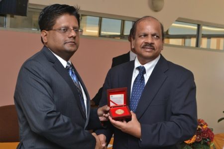 Finance Minister Dr. Ashni Singh (left) receives a copy of the commemorative coin from Bank of Guyana Governor Dr. Gobind Ganga (GINA photo)