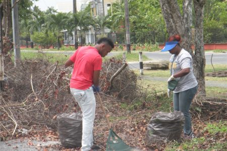 Two members of the Guyana Shines project cleaning up Waterloo Street last Sunday. (Rae Wiltshire photo)