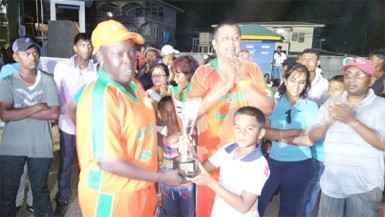 Young Richie Deonarain hands over the trophy to Erva Giddings of the Karibee Girls following their team’s defeat of Trophy Stall Angels last Sunday at Crabwood Creek.